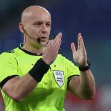 Sędzia piłkarski w jaskrawej koszulce z emblematem UEFA, gestykuluje. Ciekawe, ile zarabia sędzia piłkarski za takie emocje na boisku.
