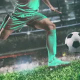 Piłkarz w zielonym stroju drybluje piłką na tle stadionu. To obraz, który przywołuje ducha legend piłki nożnej.