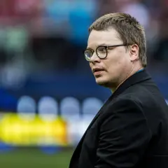 Jarosław Królewski w okularach, w czarnym garniturze, na tle stadionu.