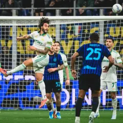 Piłkarz w białej koszulce wyskakuje do strzału głową podczas meczu Inter Mediolan – AS Roma. Piłka leci w górę.