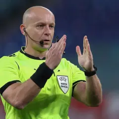 Sędzia piłkarski w jaskrawej koszulce z emblematem UEFA, gestykuluje. Ciekawe, ile zarabia sędzia piłkarski za takie emocje na boisku.