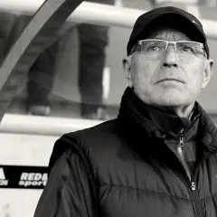 Lenczyk, trener piłkarski, w okularach i czapce z daszkiem, patrzy z uwagą.