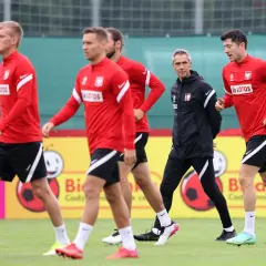 Piłkarze reprezentacji Polski w czerwonych strojach i trener w czarnej kurtce podczas treningu. Lewandowski i inni zawodnicy w akcji.