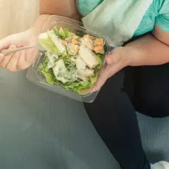 Osoba w stroju sportowym je sałatkę z kurczakiem z plastikowego pojemnika.
