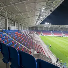 Puste trybuny stadionu Odra Opole w kolorach niebieskim i czerwonym, oświetlone nocą.