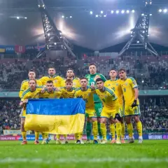 Piłkarze Ukrainy w żółtych strojach z flagą narodową przed meczem barażowym.