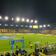 Stadion GKS Katowice podczas meczu z Górnikiem Zabrze. Trybuny wypełnione kibicami, wielka oprawa z napisem "Górniczy Klub".