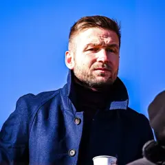 Piast Gliwice trener w granatowym płaszczu, zamyślony pod błękitnym niebem.