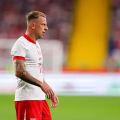 Piłkarz Kamil Grosicki w białej koszulce i czerwonych spodenkach, z tatuażami na ramieniu. Jego majątek budowany latami kariery.