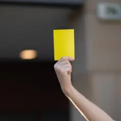 Ręka unosi żółtą kartkę. Może to symbol ostrzeżenia lub przypomnienia.