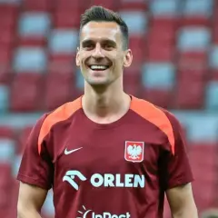 Uśmiechnięty piłkarz w koszulce reprezentacji Polski, mimo że jego **milik kontuzja** mogła go martwić, wygląda na zrelaksowanego.
