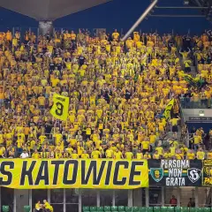 Tłum kibiców GKS Katowice w żółtych barwach, z transparentem "GKS KATOWICE" i flagami.