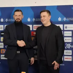 Dwóch mężczyzn w garniturach ściska sobie dłonie na tle ścianki sponsorskiej Rakowa Częstochowa. Zapowiada to nowe, ekscytujące transfery!