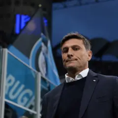 Trener piłkarzy z Mediolanu, z flagami Interu w tle, gotowy do meczu.