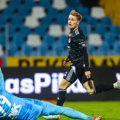 Piłkarz w czarnej koszulce biegnie, bramkarz ŁKS Łódź w błękitnym stroju broni strzał. Przebieg: Stal Mielec – ŁKS Łódź.