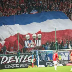 Oprawa meczu Ruch Chorzów – Wisła Kraków. Ogromna flaga w barwach biało-czerwono-niebieskich zakrywa trybuny, a pod nią bębny i kibice.