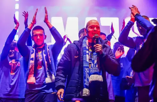 Mężczyzna z mikrofonem, otoczony przez młodych ludzi w szalikach, świętuje sukces jako mistrz polski ekstraklasa.
