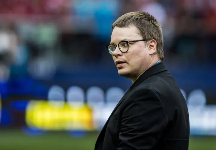 Jarosław Królewski w okularach, w czarnym garniturze, na tle stadionu.
