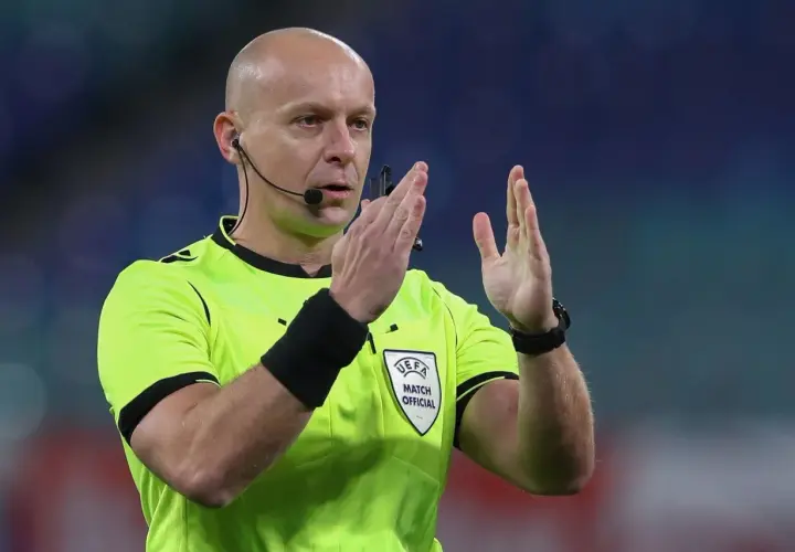 Sędzia piłkarski w jaskrawej koszulce z emblematem UEFA, gestykuluje. Ciekawe, ile zarabia sędzia piłkarski za takie emocje na boisku.