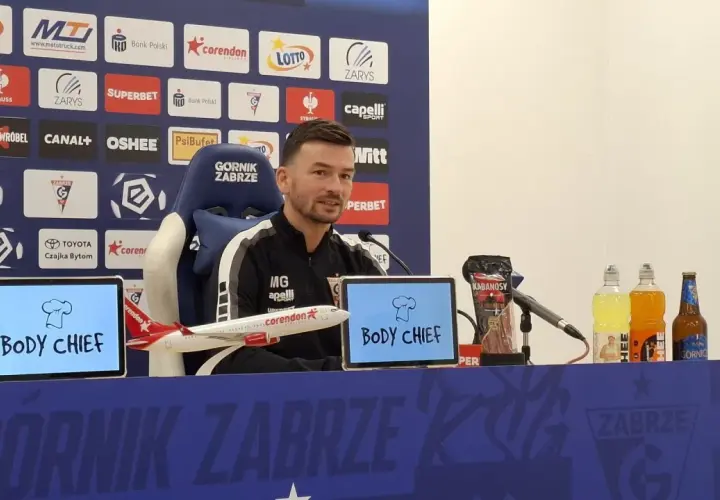 Trener Górnika Zabrze przed meczem z Rakowem Częstochowa. Na stole kabanosy, napoje i model samolotu.