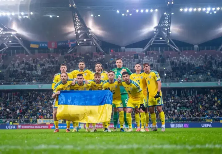 Piłkarze Ukrainy w żółtych strojach z flagą narodową przed meczem barażowym.