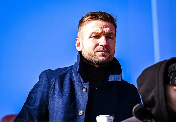 Piast Gliwice trener w granatowym płaszczu, zamyślony pod błękitnym niebem.
