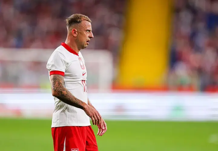 Piłkarz Kamil Grosicki w białej koszulce i czerwonych spodenkach, z tatuażami na ramieniu. Jego majątek budowany latami kariery.