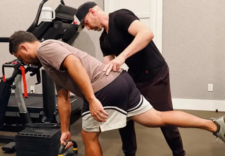 Trener pomaga mężczyźnie w ćwiczeniu rozciągającym biodro z kettlebell.