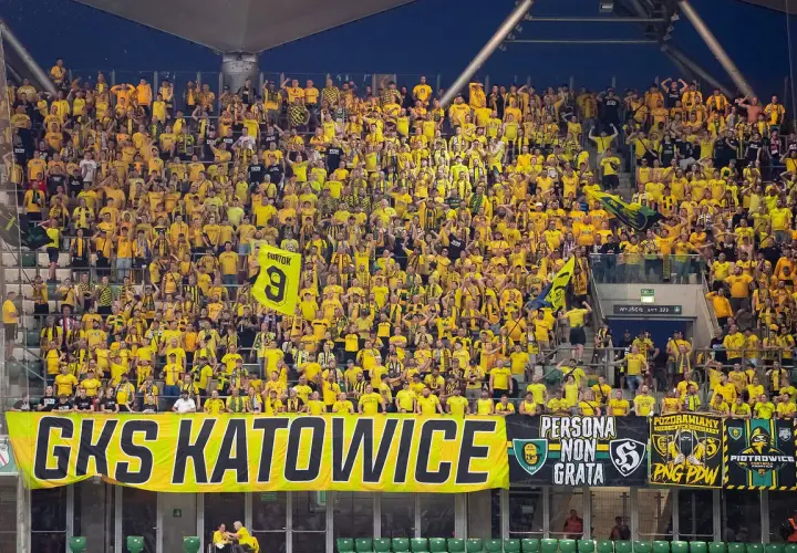 Tłum kibiców GKS Katowice w żółtych barwach, z transparentem "GKS KATOWICE" i flagami.