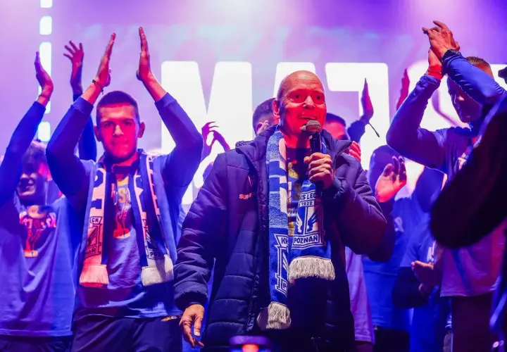 Mężczyzna z mikrofonem, otoczony przez młodych ludzi w szalikach, świętuje sukces jako mistrz polski ekstraklasa.