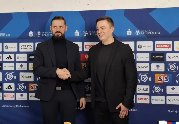 Dwóch mężczyzn w garniturach ściska sobie dłonie na tle ścianki sponsorskiej Rakowa Częstochowa. Zapowiada to nowe, ekscytujące transfery!