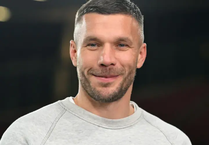 Uśmiechnięty Lukas Podolski w szarej bluzie. Jego majątek budowany latami kariery piłkarskiej i biznesów.