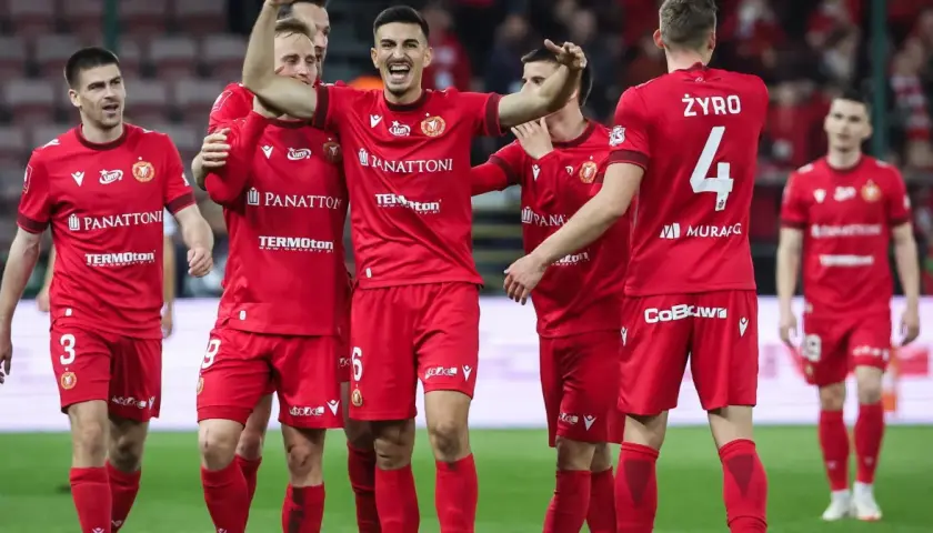 Piłkarze Widzewa Łódź w czerwonych strojach świętują na boisku.