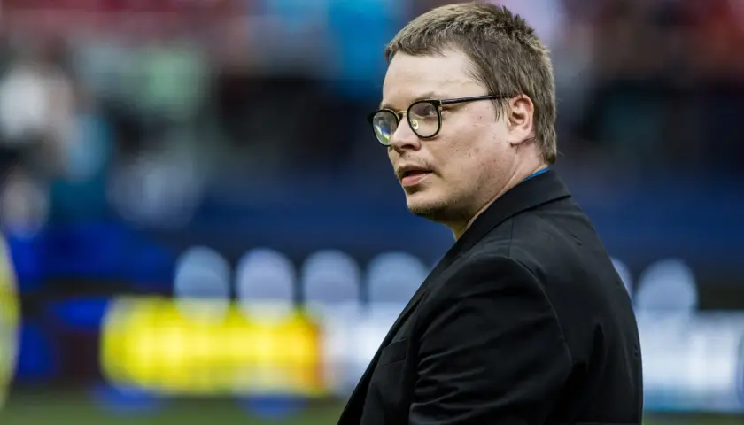 Jarosław Królewski w okularach, w czarnym garniturze, na tle stadionu.