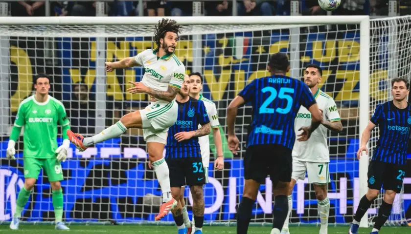 Piłkarz w białej koszulce wyskakuje do strzału głową podczas meczu Inter Mediolan – AS Roma. Piłka leci w górę.