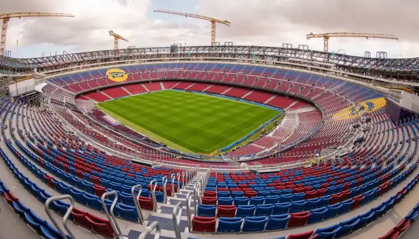Widok na budowane nowe Camp Nou. Krzesełka w kolorach czerwonym i niebieskim czekają na kibiców, a nad stadionem górują dźwigi.