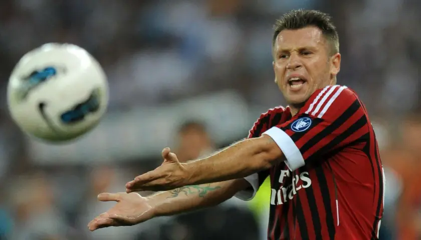 Piłkarz Cassano w koszulce Milanu, z wyrazem frustracji na twarzy, gestykuluje w stronę lecącej piłki.