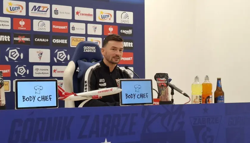 Trener Górnika Zabrze przed meczem z Rakowem Częstochowa. Na stole kabanosy, napoje i model samolotu.