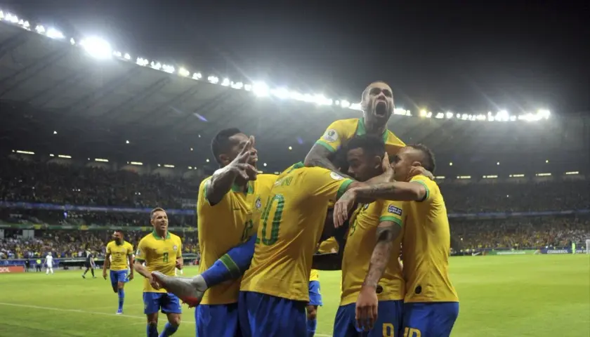 Piłkarze Brazylii świętują zwycięstwo nad Argentyną. Stadion wypełniony kibicami, nocne światła oświetlają murawę.