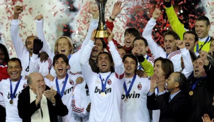 Piłkarze AC Milan świętują z pucharem, w tle konfetti i dym.