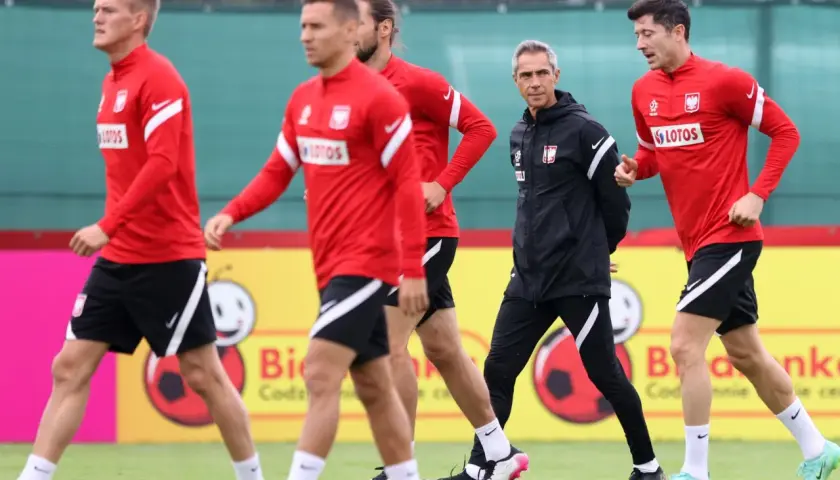 Piłkarze reprezentacji Polski w czerwonych strojach i trener w czarnej kurtce podczas treningu. Lewandowski i inni zawodnicy w akcji.