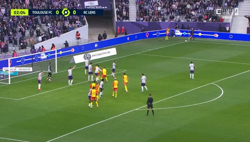Mecz Toulouse FC - RC Lens. Piłkarze w białych i żółtych strojach szykują się do akcji pod bramką.