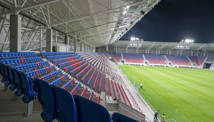 Puste trybuny stadionu Odra Opole w kolorach niebieskim i czerwonym, oświetlone nocą.