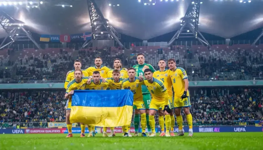 Piłkarze Ukrainy w żółtych strojach z flagą narodową przed meczem barażowym.