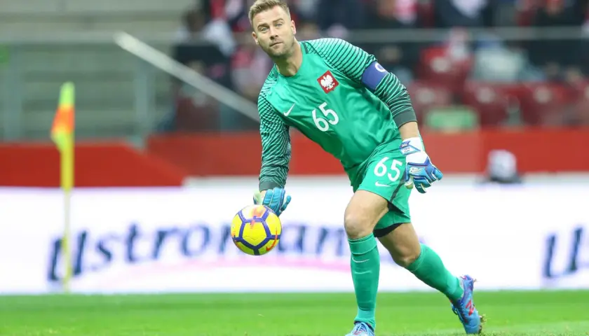 Bramkarz w zielonym stroju z numerem 65, z piłką w ręce, gotowy do akcji. Borubar czuwa nad bramką.