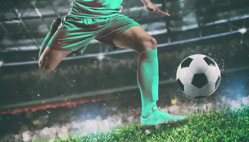 Piłkarz w zielonym stroju drybluje piłką na tle stadionu. To obraz, który przywołuje ducha legend piłki nożnej.