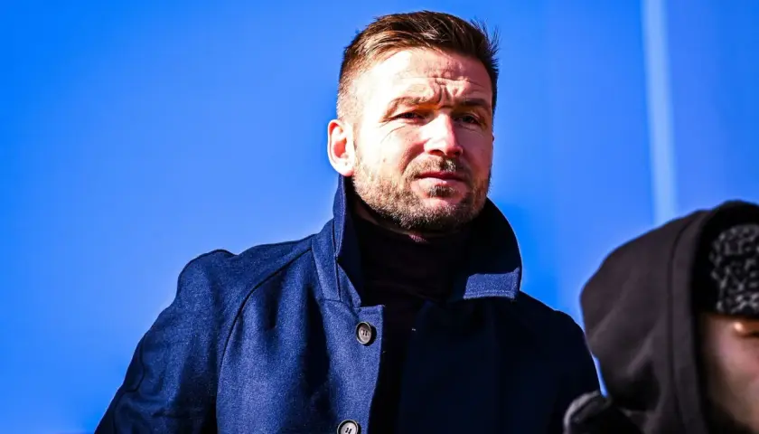 Piast Gliwice trener w granatowym płaszczu, zamyślony pod błękitnym niebem.