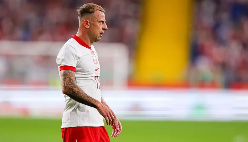 Piłkarz Kamil Grosicki w białej koszulce i czerwonych spodenkach, z tatuażami na ramieniu. Jego majątek budowany latami kariery.