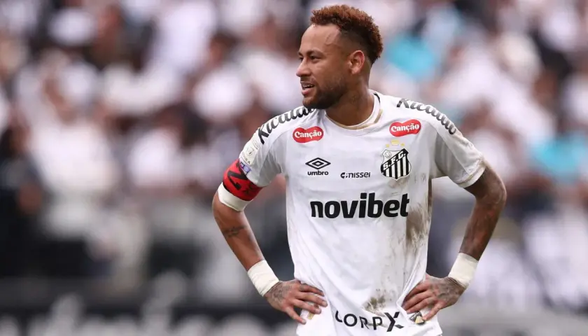 Neymar w białej koszulce Santos FC, z opaską kapitana na ramieniu, na tle trybun.