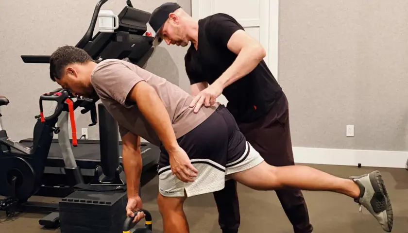 Trener pomaga mężczyźnie w ćwiczeniu rozciągającym biodro z kettlebell.